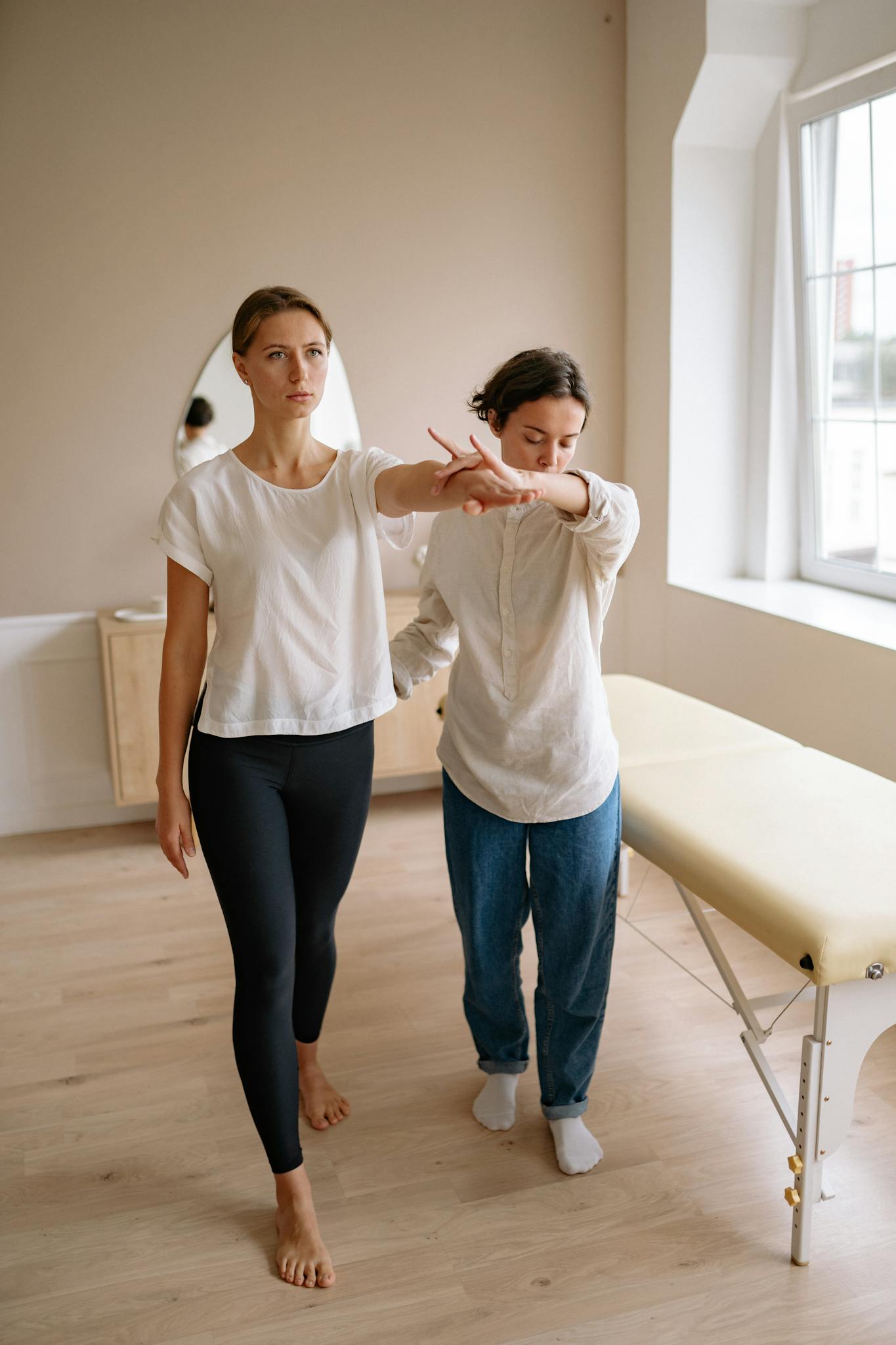 A therapeutic session where a therapist assists a client near a massage table indoors.